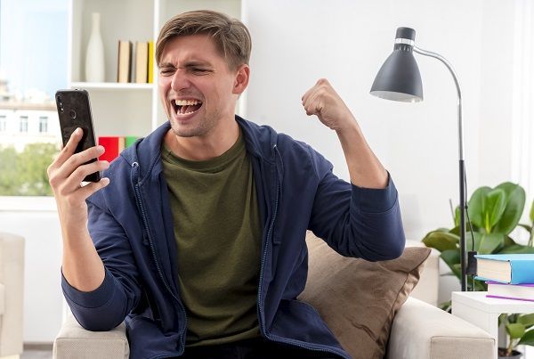 Hombre mirando el móvil con el puño levantado indicando emoción en la apuesta