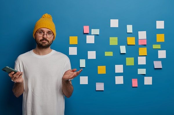 Hombre con las manos ligeramente levantados indicando que no entiende el funcionamiento de algo con muchos post-it detrás en la pared