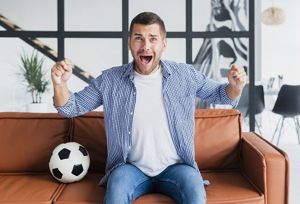 Hombre levantando los brazos celebrando un gol con un balón de fútbol