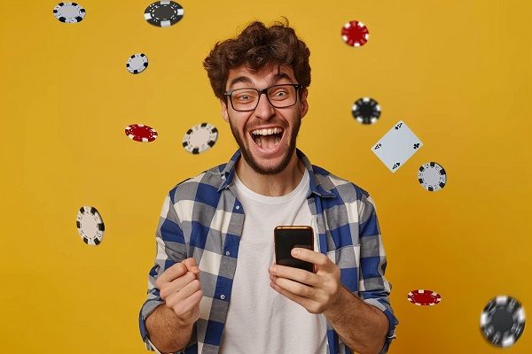Hombre feliz con su móvil en la mano comenzando con su bono de apuestas y fichas volando