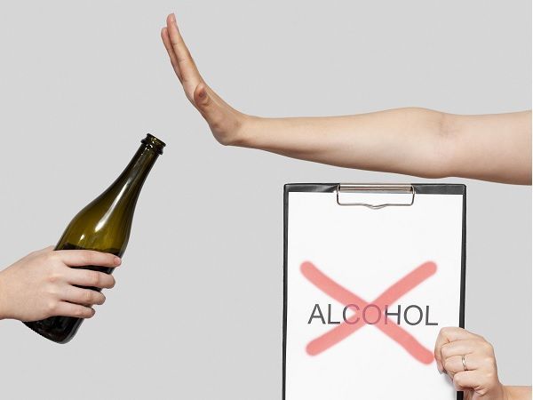 Mano diciendo no a una botella con un letrero con la palabra alcohol tachada