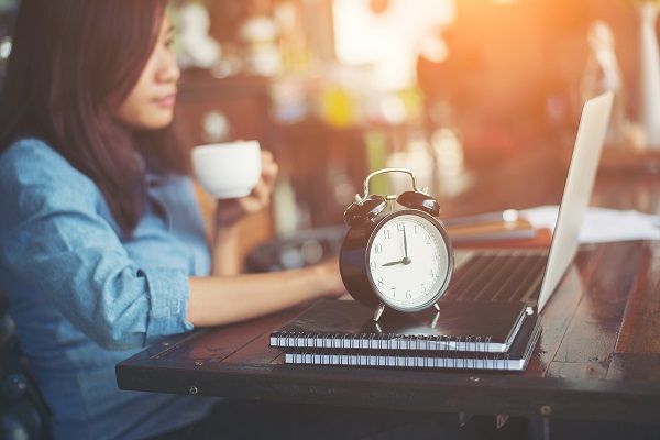 Mujer delante de ordenador con reloj al lado representando la gestión de tiempo