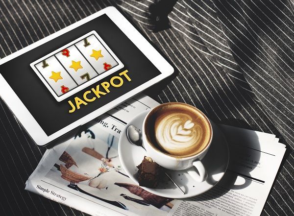 Tablet encendida con manual de jackpot junto taza de café y periódico