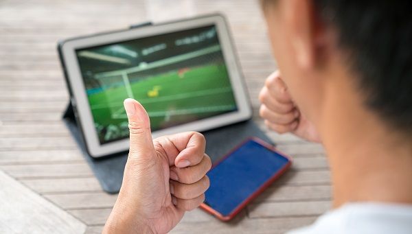 Hombre con pulgares arriba viendo partido en tablet representando el aprendizaje de apuestas