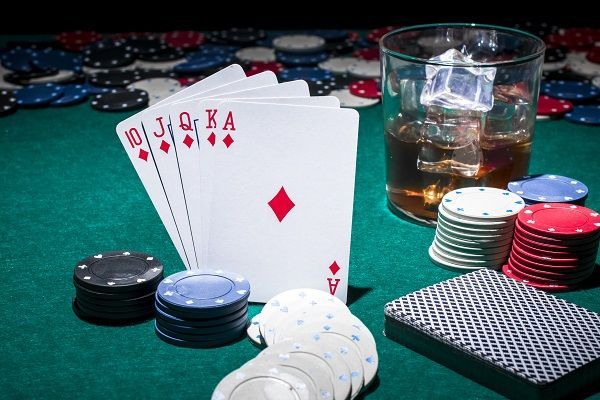 Mano de póker en la mesa junto a bebida, cartas y fichas